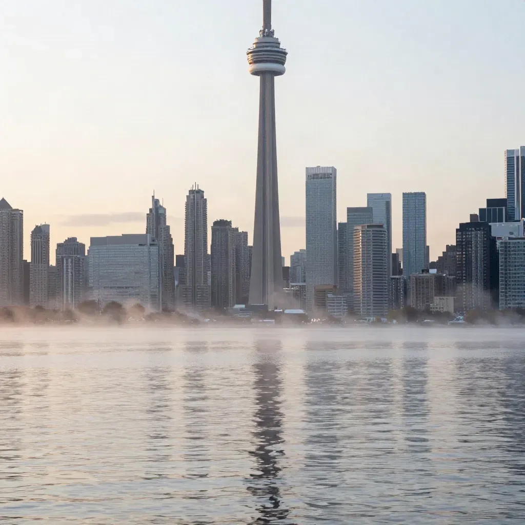 Toronto skyline with CN Tower above calm lake haze at dawn